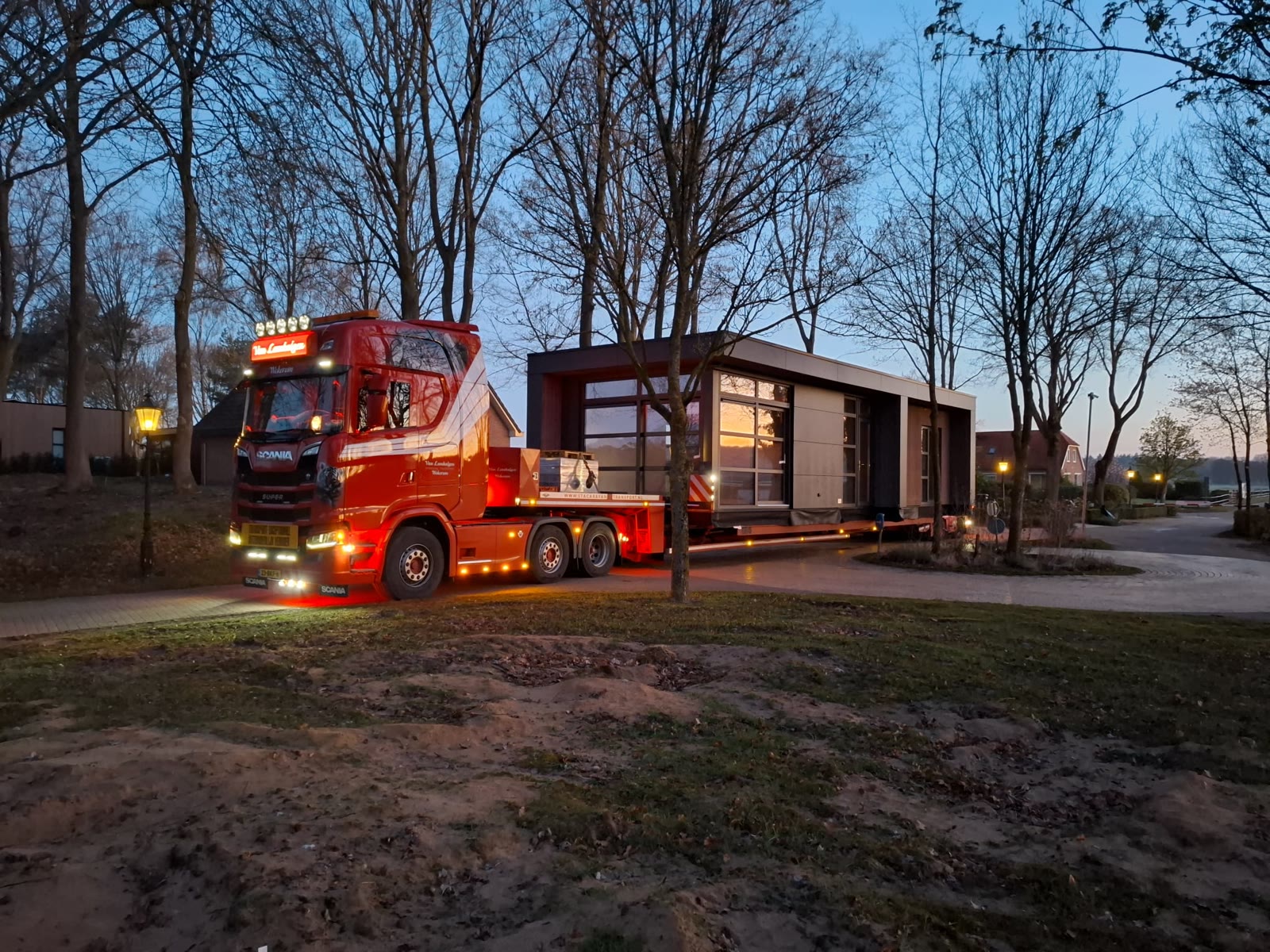 Rode truck met een modern chalet op de oplegger in de schemering op een vakantiepark