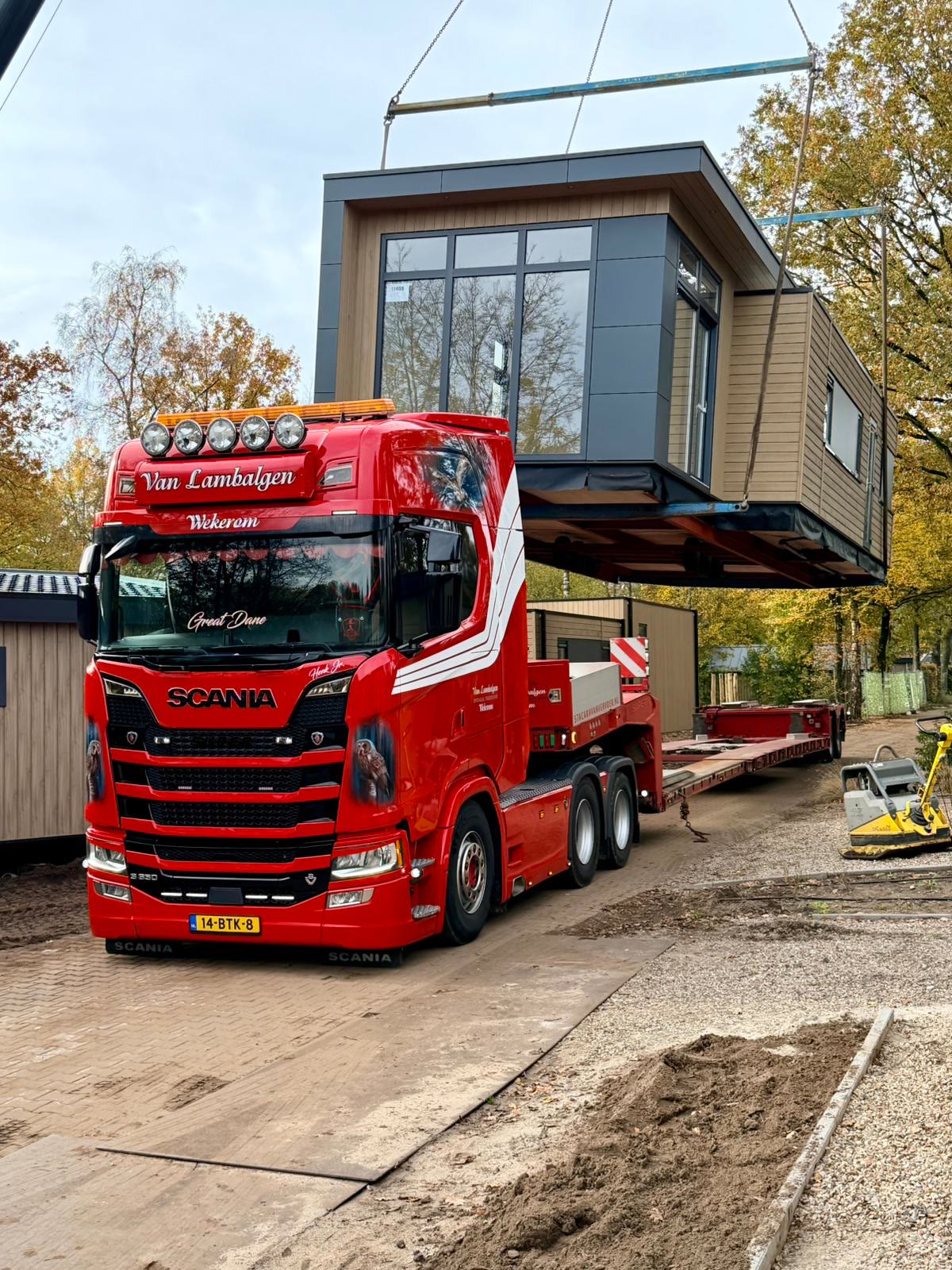Kraan tilt een moderne woning van de oplegger van een rode Van Lambalgen truck